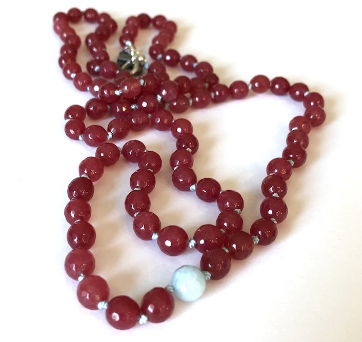 Raspberry colored, faceted jade gemstone necklace, hand knotted on pale blue silk and finished with silver clasp. Has one amazonite bead.